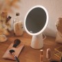 Weiße Philips LED Tischleuchte Mirror mit Spiegel auf einem Tisch mit Kosmetikartikeln.