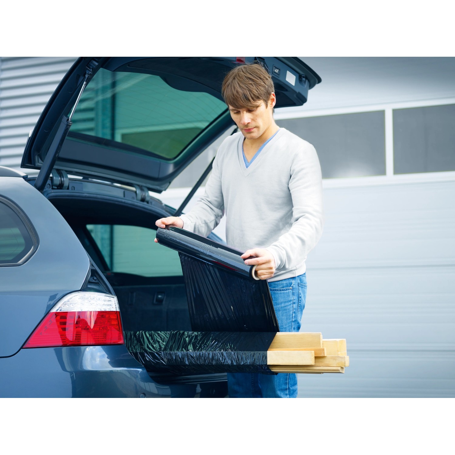 Mann verpackt Holz mit schwarzer LUX Stretchfolie im Kofferraum eines Autos.