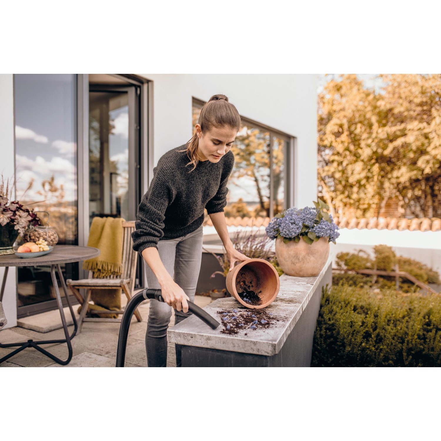 Frau saugt Erde mit Kärcher Nass-/Trockensauger WD 3 S V-17/4/20 auf Terrasse.