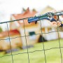 Rapid Zaunzange FP222 beim Befestigen von Spanndraht an einem grünen Gartenzaun.
