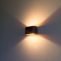 Rechteckige, schwarze Wandleuchte mit goldenem Reflektor, die warmes Licht nach oben und unten wirft.