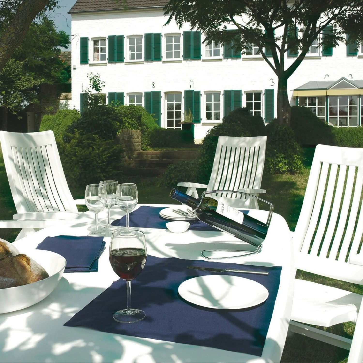 Weiße Kettler ROMA Multipositionssessel aus Kunststoff an Gartentisch mit Wein und Brot. Gartenmöbel für entspannte Stunden.