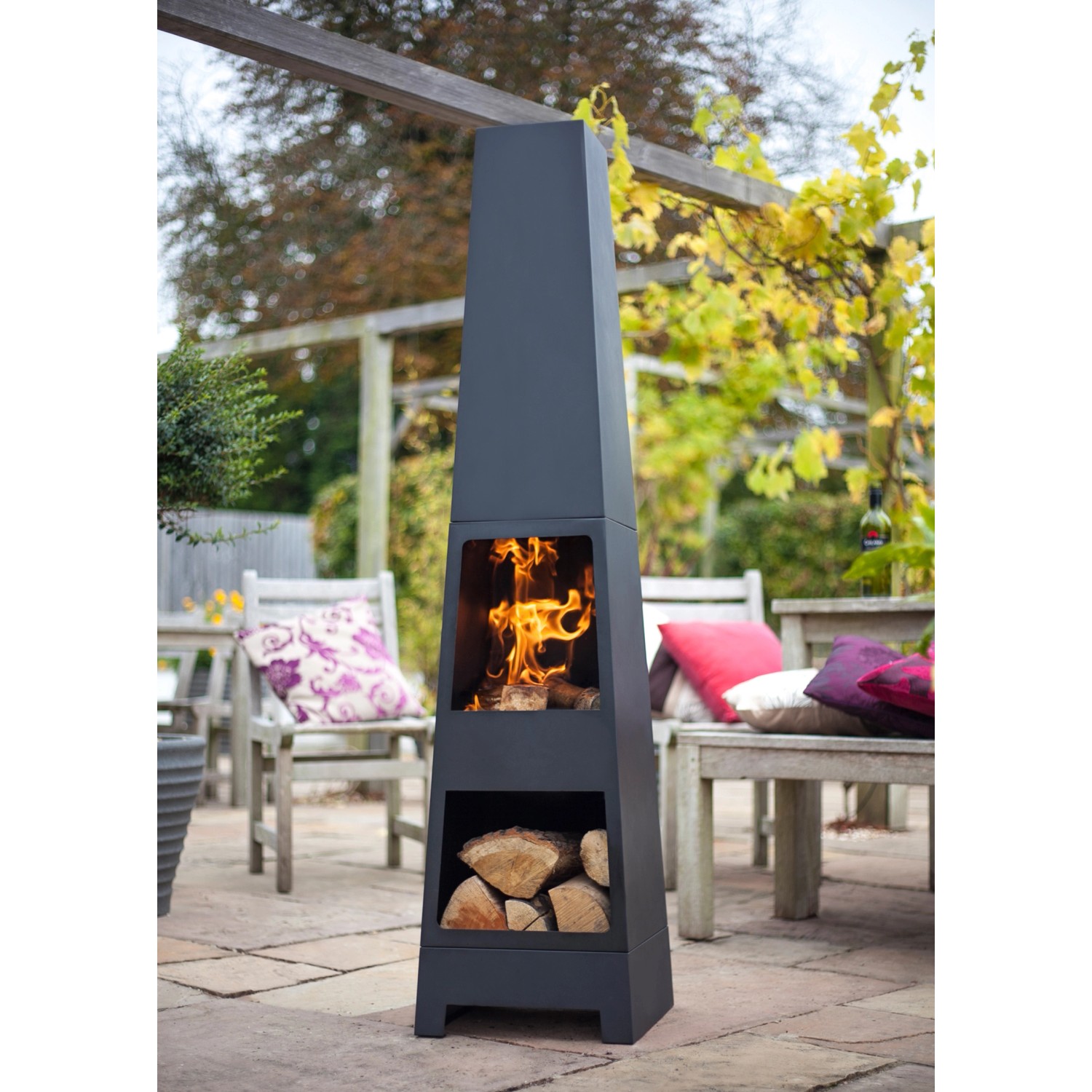 Schwarzer Buschbeck Gartenkamin Malmo mit Holzfach und Feuerstelle im Garten.