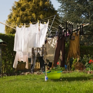 Silberne Relaxdays Bodenhülse aus Stahl mit Wäschespinne und aufgehängter Wäsche im Garten.