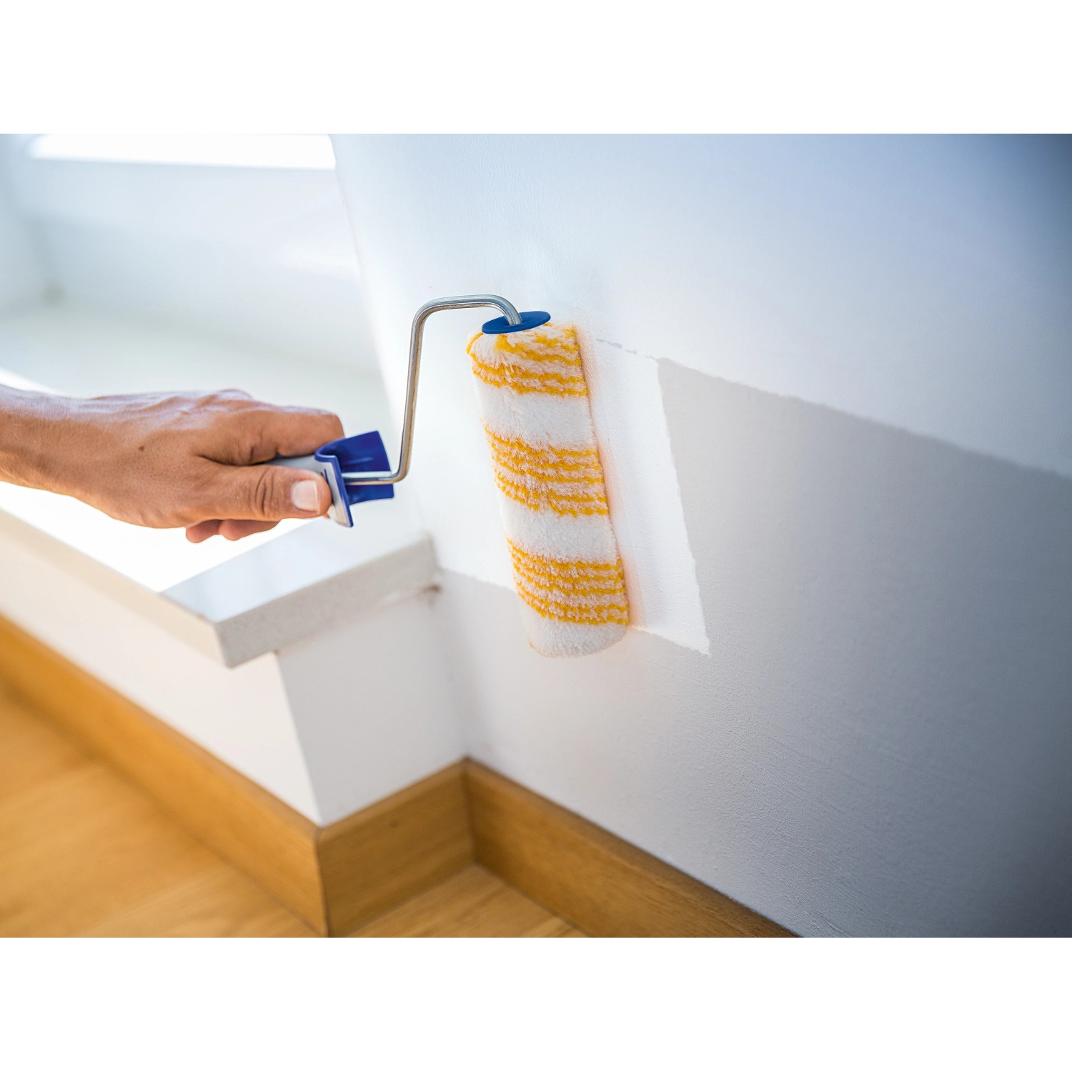 LUX Dispersionswalze 15 cm beim Streichen einer Wand. Farbwalze mit gelben Streifen und blauem Griff.
