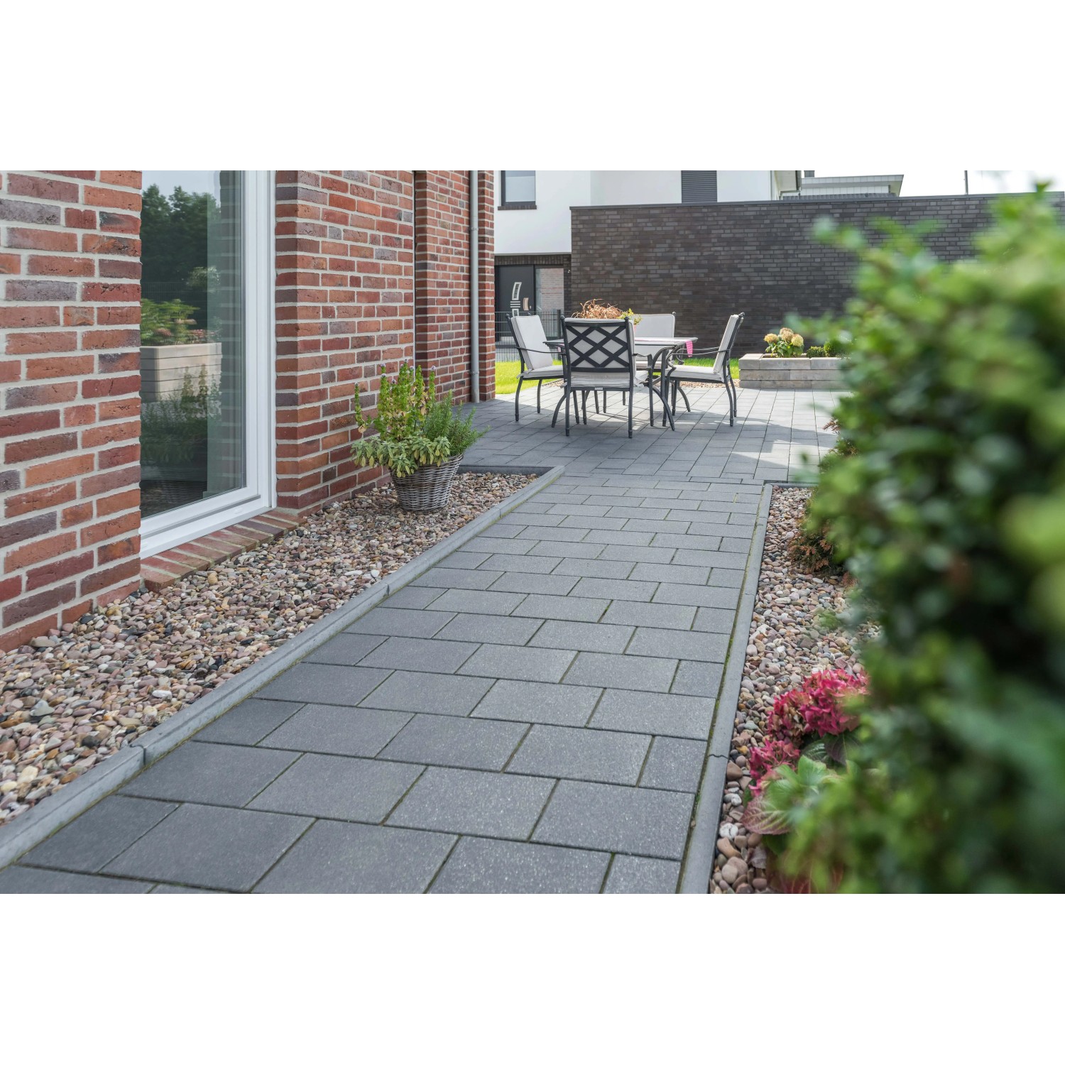 Diephaus Kantenstein Basalt mit Glimmer, eingefasster Gartenweg mit Sitzgruppe im Hintergrund.