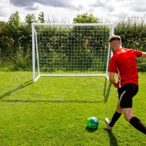 Weißes Fußballtor 2.4m x 1.8m mit Torwand und Tragetasche, Fußballspieler schießt Ball.
