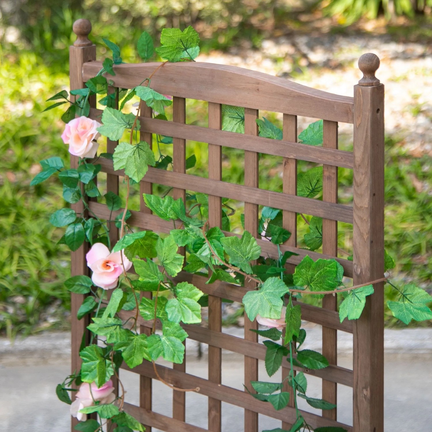 Dunkelbraunes Tannenholz-Spalier mit grünen Ranken und rosa Blüten. Ideal für Garten und Balkon.
