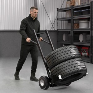 Mann schiebt schwarze Wiltec Reifenkarre mit zwei Autoreifen in Werkstatt. Ideal für Reifentransport bis 200kg.