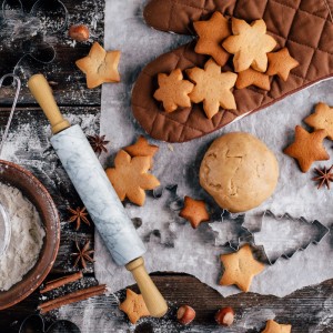 Weißes Marmor-Nudelholz mit Holzgriffen in einer Backszene mit Plätzchen, Teig und Ausstechformen auf Holztisch.