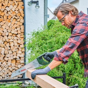 Mann sägt Holz mit Bosch Handsäge DIY 400 mm im Garten.