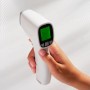 Hand hält weißen, digitalen Fieberthermometer mit grünem Display.