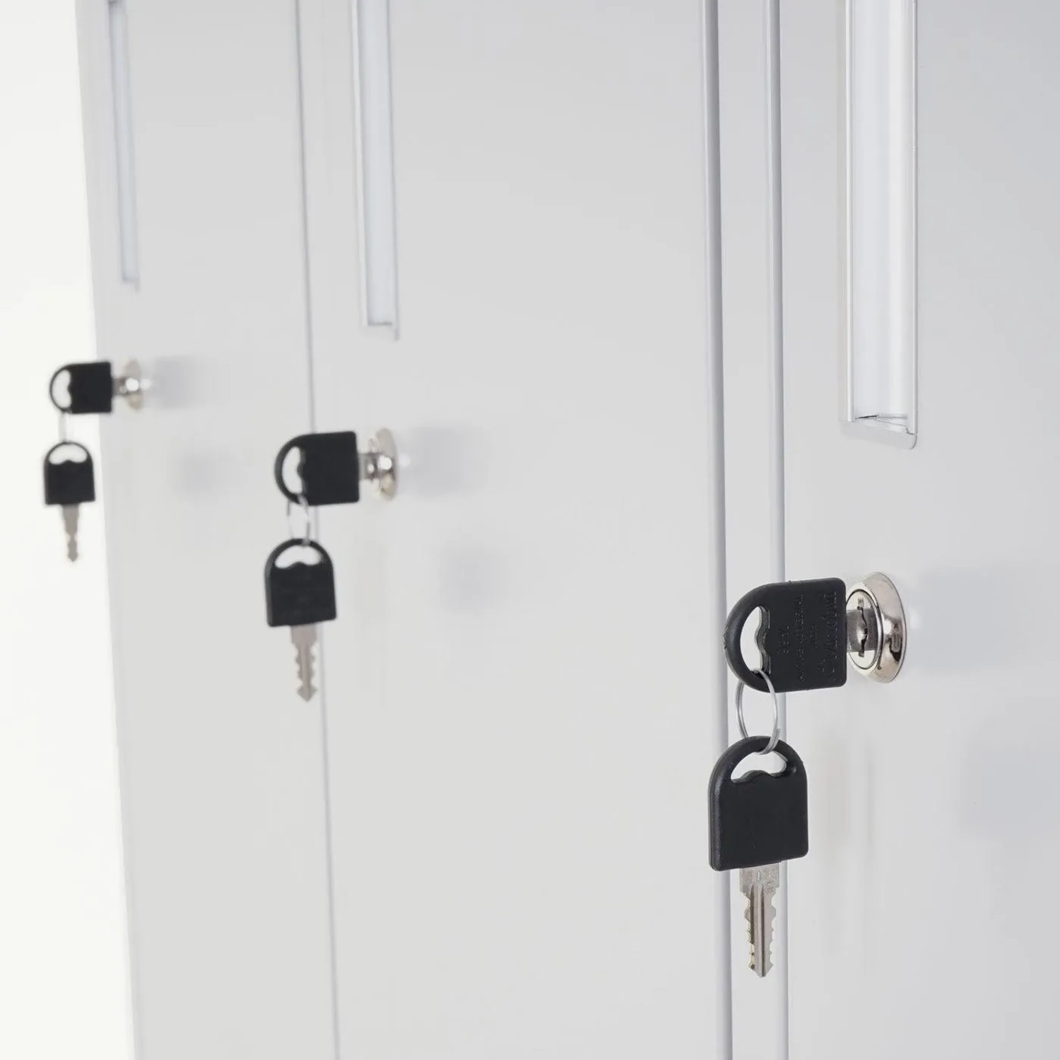 Drei helle Metall-Schließfächer mit Schlüsseln in den Drehriegelschlössern. Detail des sicheren Spind-Verschlusses für Wertfachschrank.
