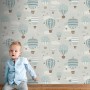 ESTAhome Tapete mit blauen Luftballons und Wolken, spielerisches Design für Kinderzimmer. Ein Kind sitzt auf einer Bank.
