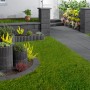 Anthrazitfarbene Gartenmauer mit Abdeckplatten und passenden Einfassungen in einem gestalteten Garten.