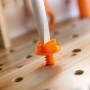 Nahaufnahme einer orangefarbenen Spielzeugschraube, die mit einem Holzschraubendreher in eine Kinderwerkbank aus Holz gedreht wird.