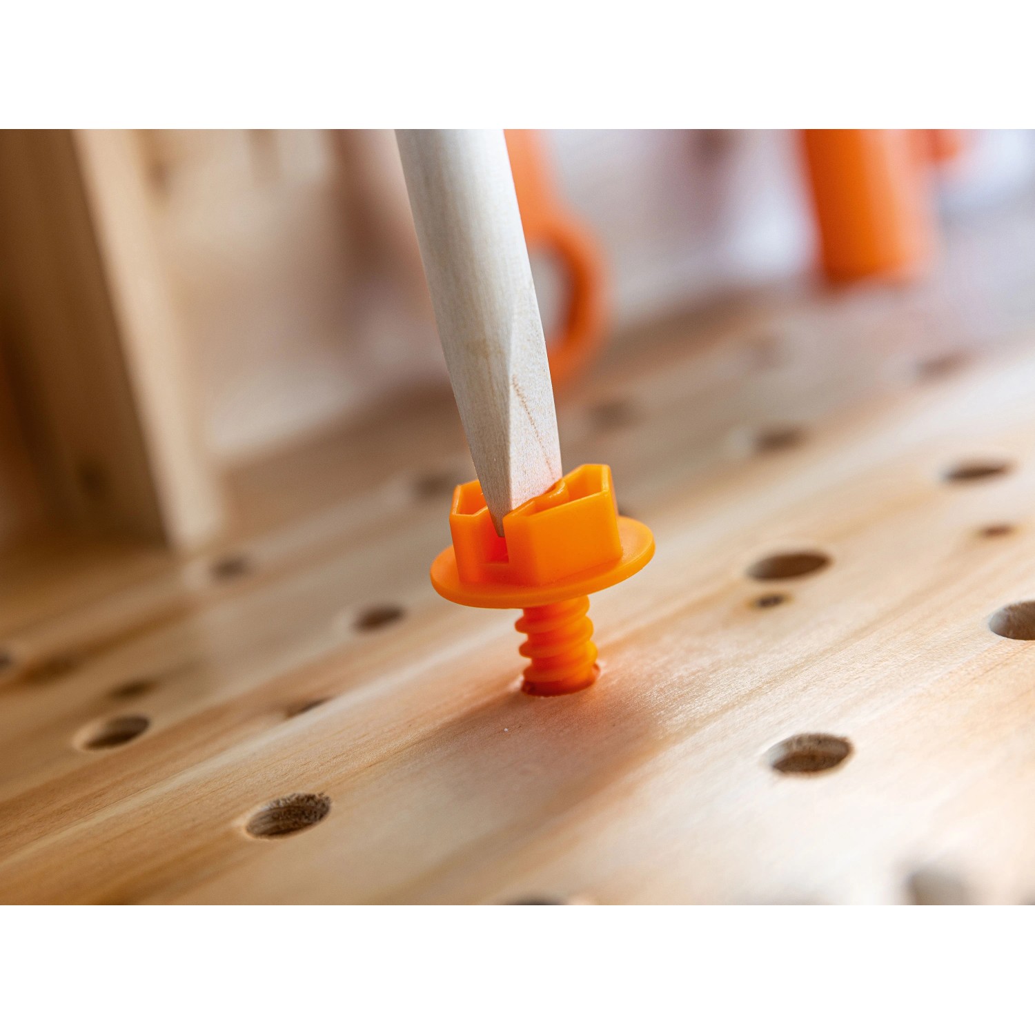Nahaufnahme einer orangefarbenen Spielzeugschraube, die mit einem Holzschraubendreher in eine Kinderwerkbank aus Holz gedreht wird.
