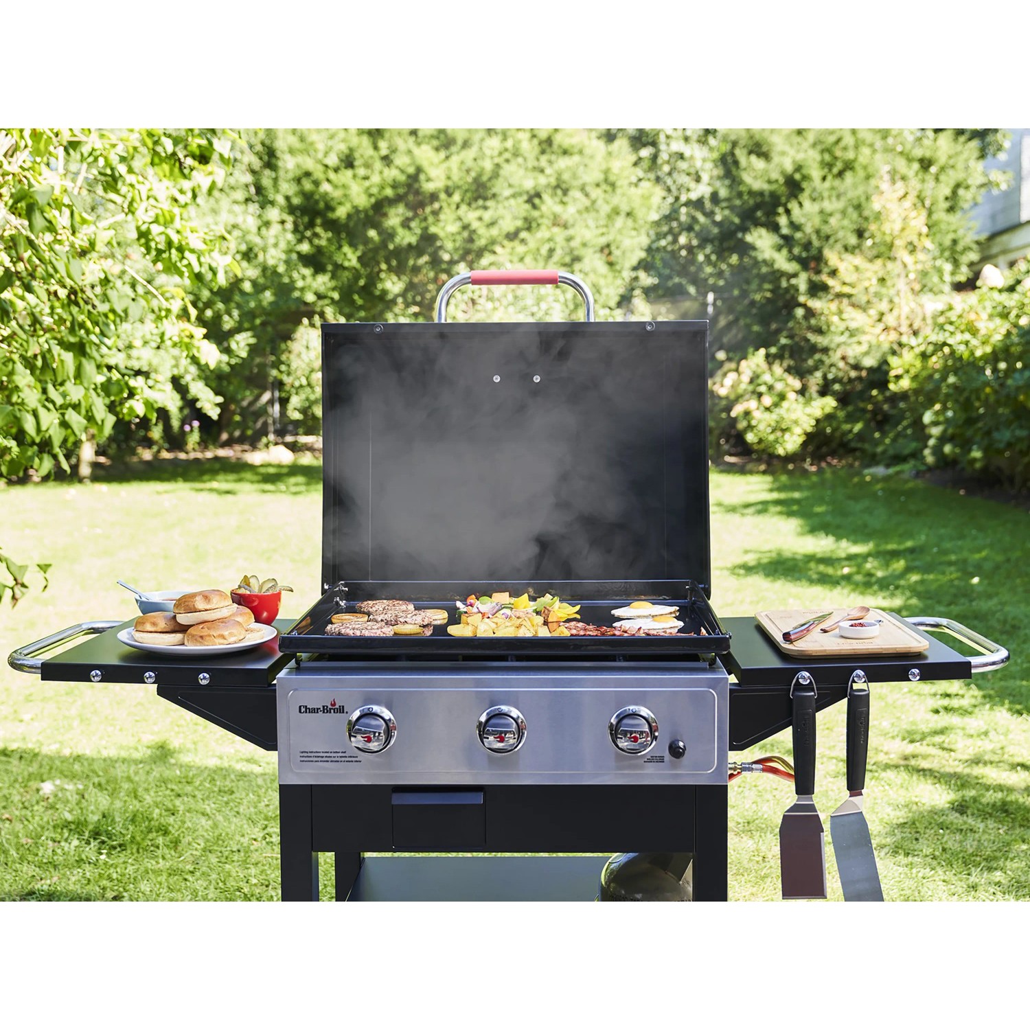Char-Broil Griddle 3400 Gasgrill mit Gusseisenplatte, Speisen und Zubehör auf Ablageflächen.