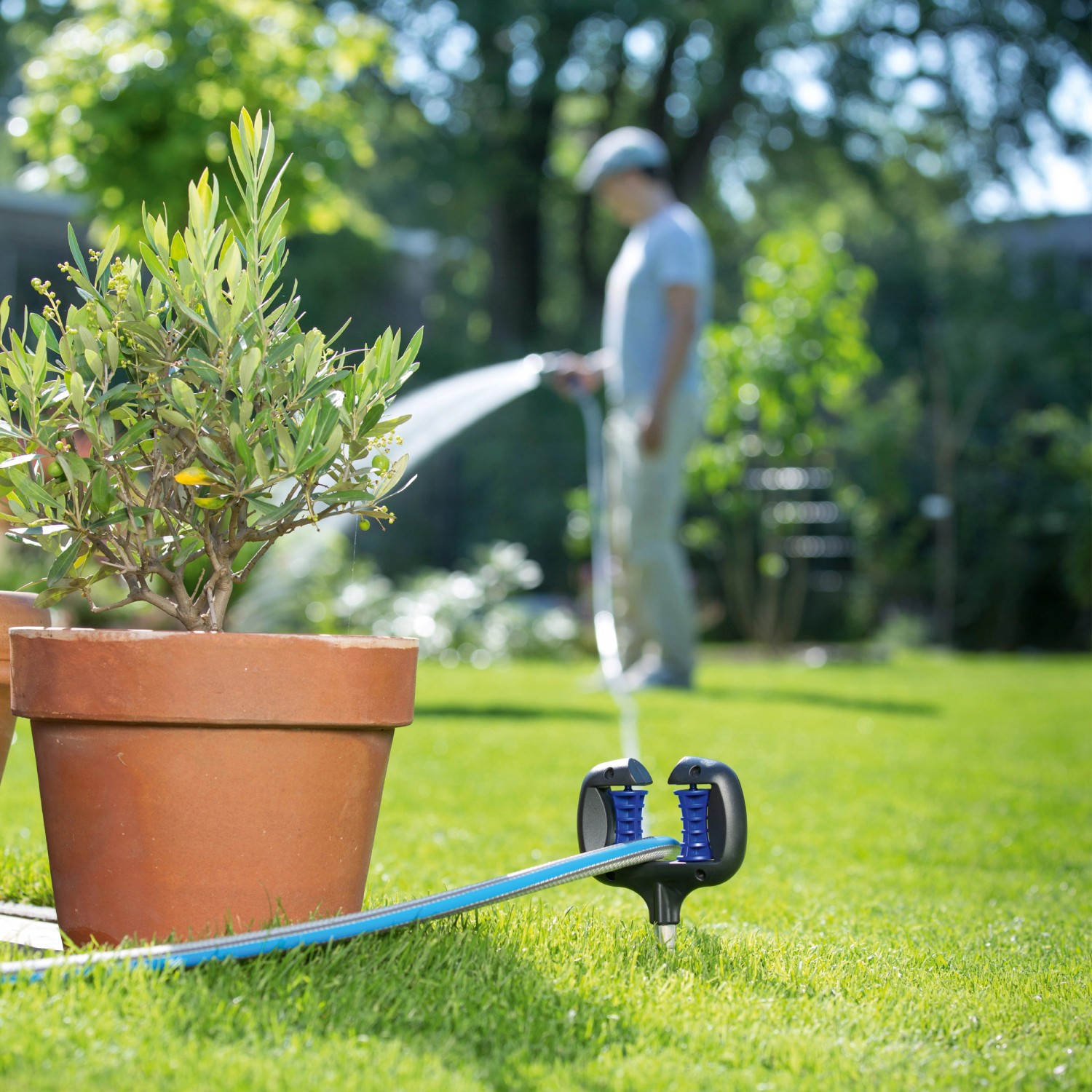LUX Schlauch- und Kabelführung im Garten mit Schlauch und Erdspieß. Person bewässert Pflanzen.