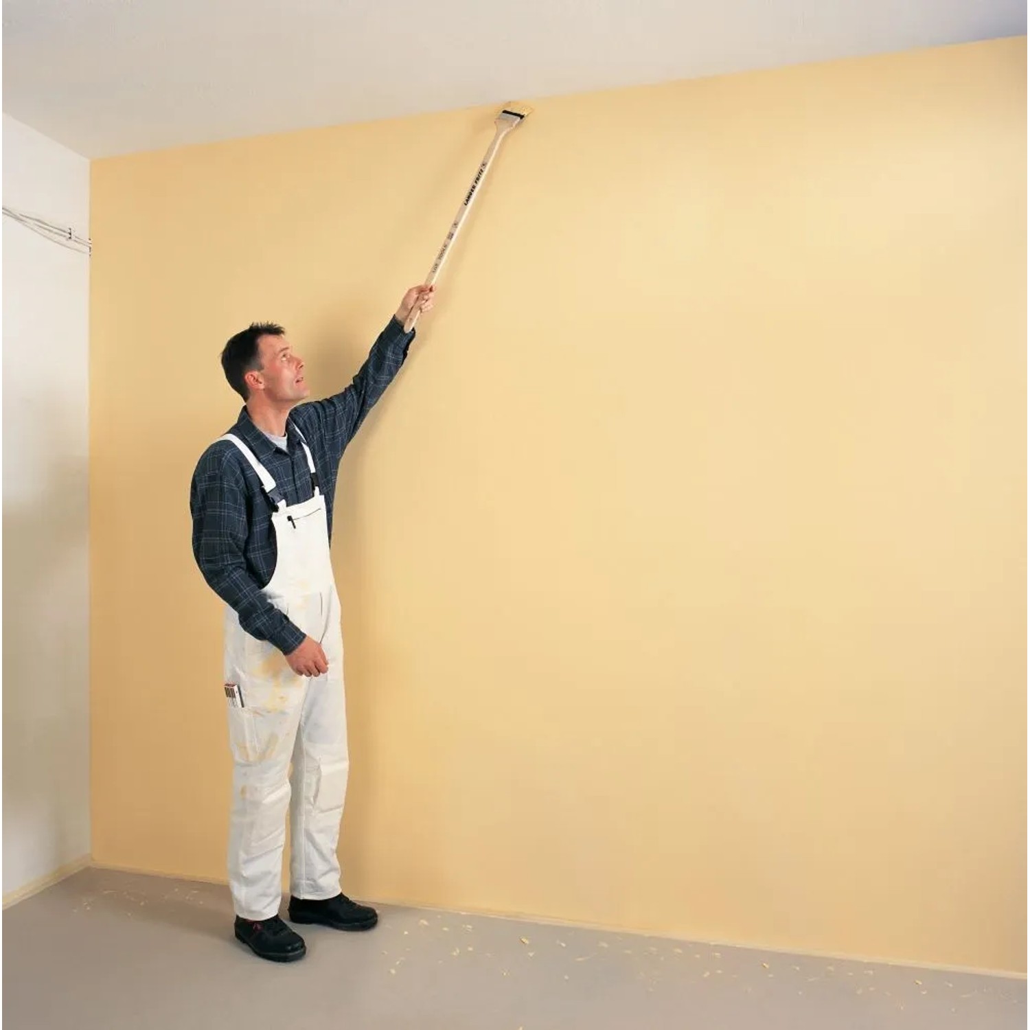 Mann streicht Wand mit Fassadenpinsel Langer Fritz 75 mm mit langem Griff.