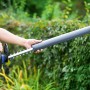 LUX Elektro-Heckenschere E-HS-600/55 A mit Messerschutz vor grüner Hecke.