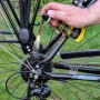 Hand sprüht Ballistol Keramik-Kettenöl auf Fahrradkette und Ritzel. Fahrradpflege für ruhigen Lauf.