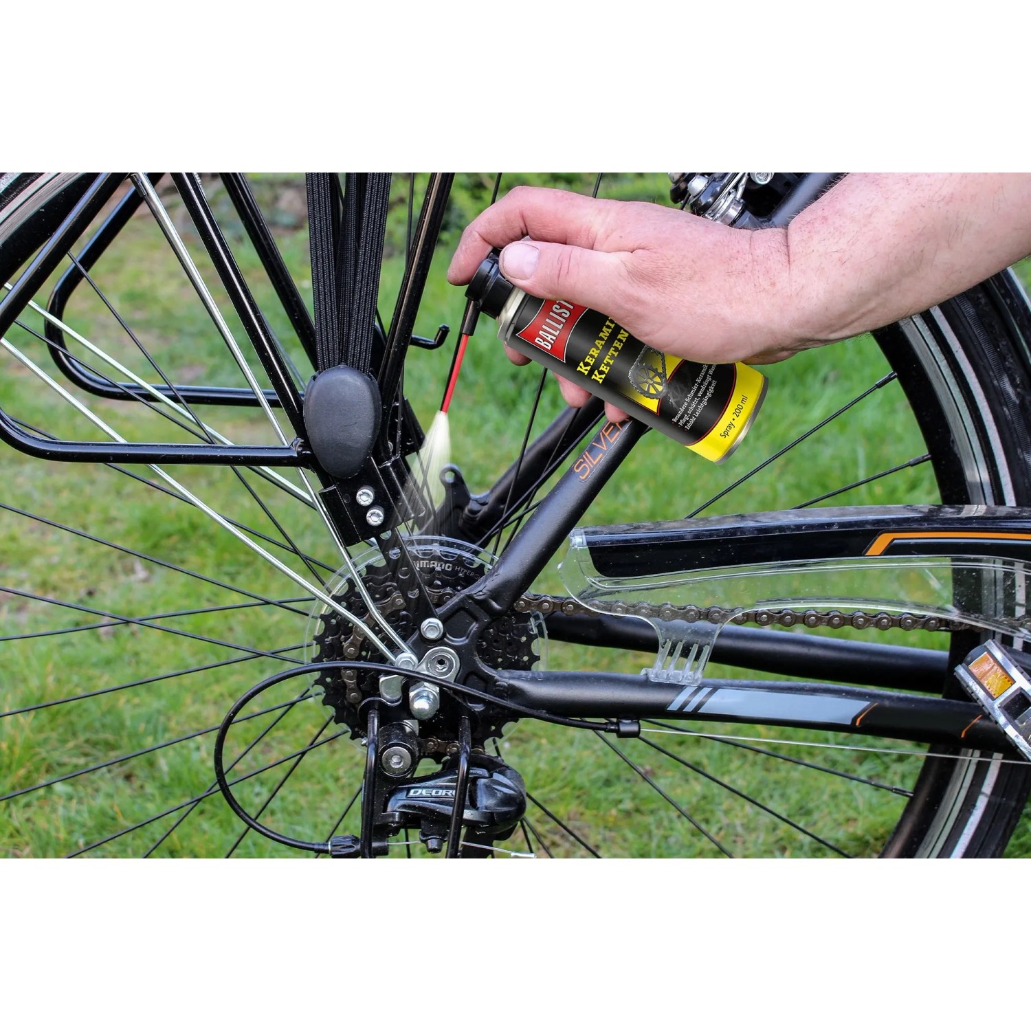 Hand sprüht Ballistol Keramik-Kettenöl auf Fahrradkette und Ritzel. Fahrradpflege für ruhigen Lauf.