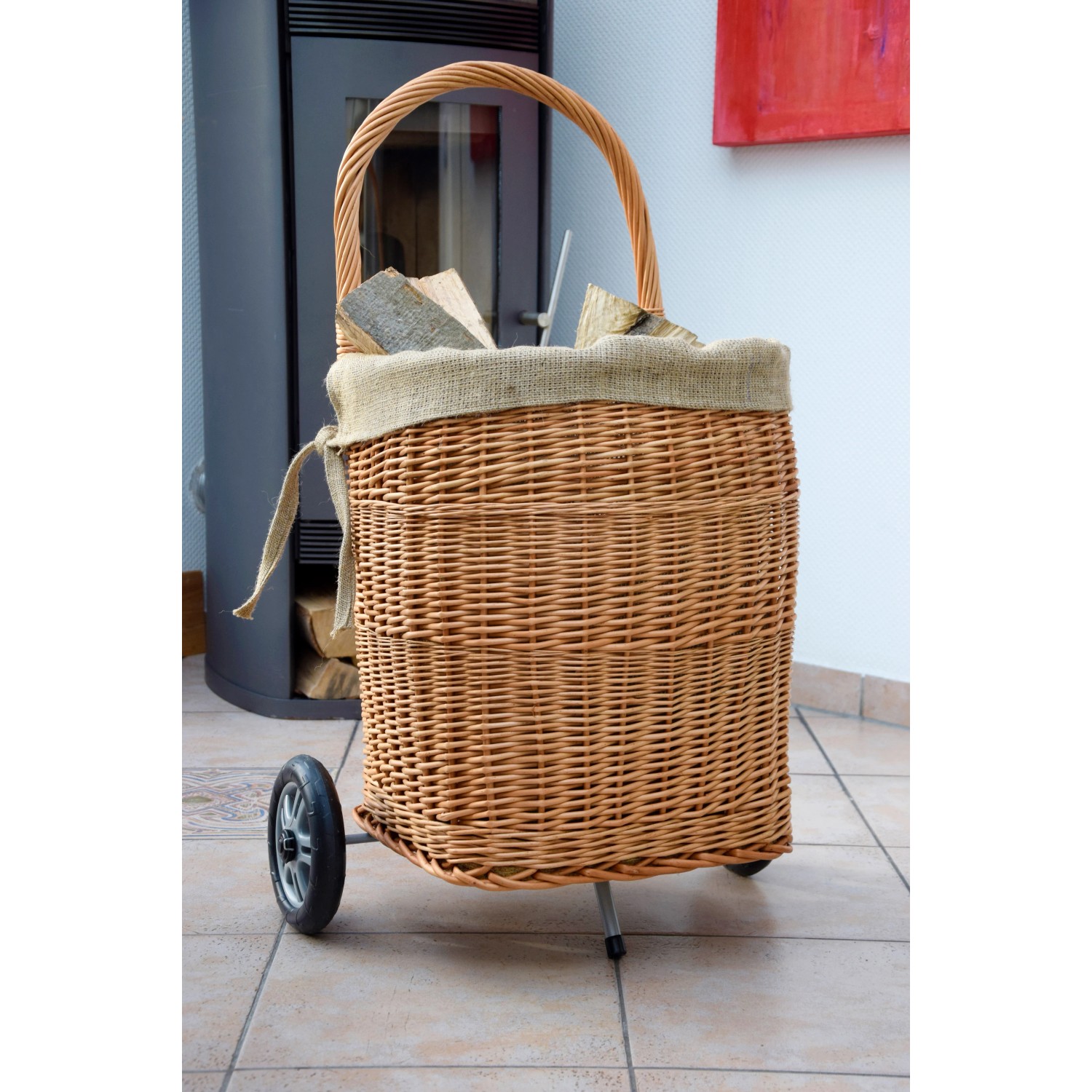 Kaminholzwagen aus Weide mit Rädern, gefüllt mit Holz, vor Kaminofen. Zubehör für Kamine.