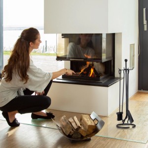 Schwarzes 5-teiliges Kaminbesteck aus Stahl auf Ständer neben modernem Kamin. Kaminzubehör mit Schürhaken, Besen, Schaufel, Zange.