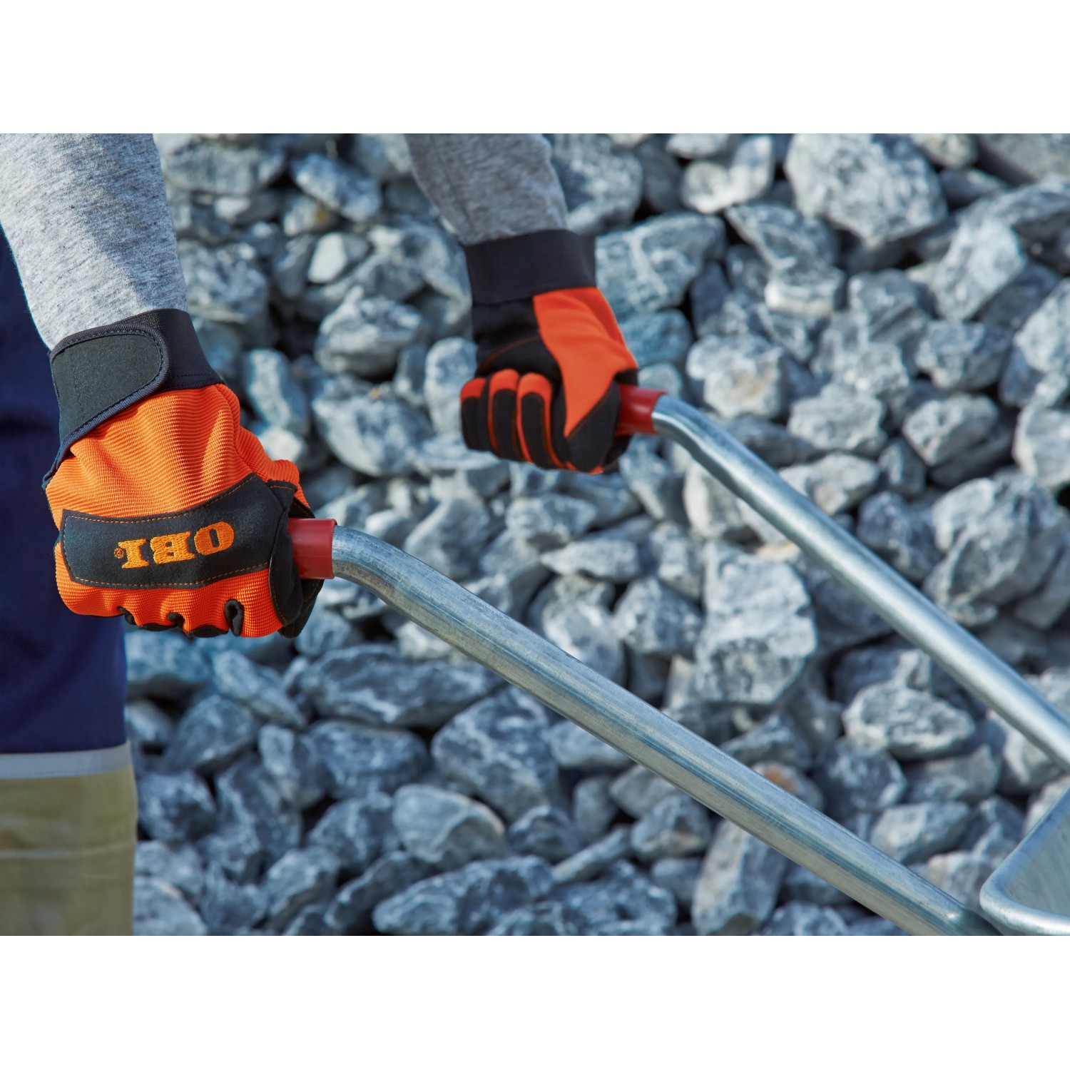 Hände mit OBI Arbeitshandschuhen (Größe 10) halten eine Schubkarre vor Steinen.