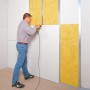 Mann montiert Dachausbau-Komplettpaket WLG 035 mit Mineralfaser Dämmstoffen an einer Wand.