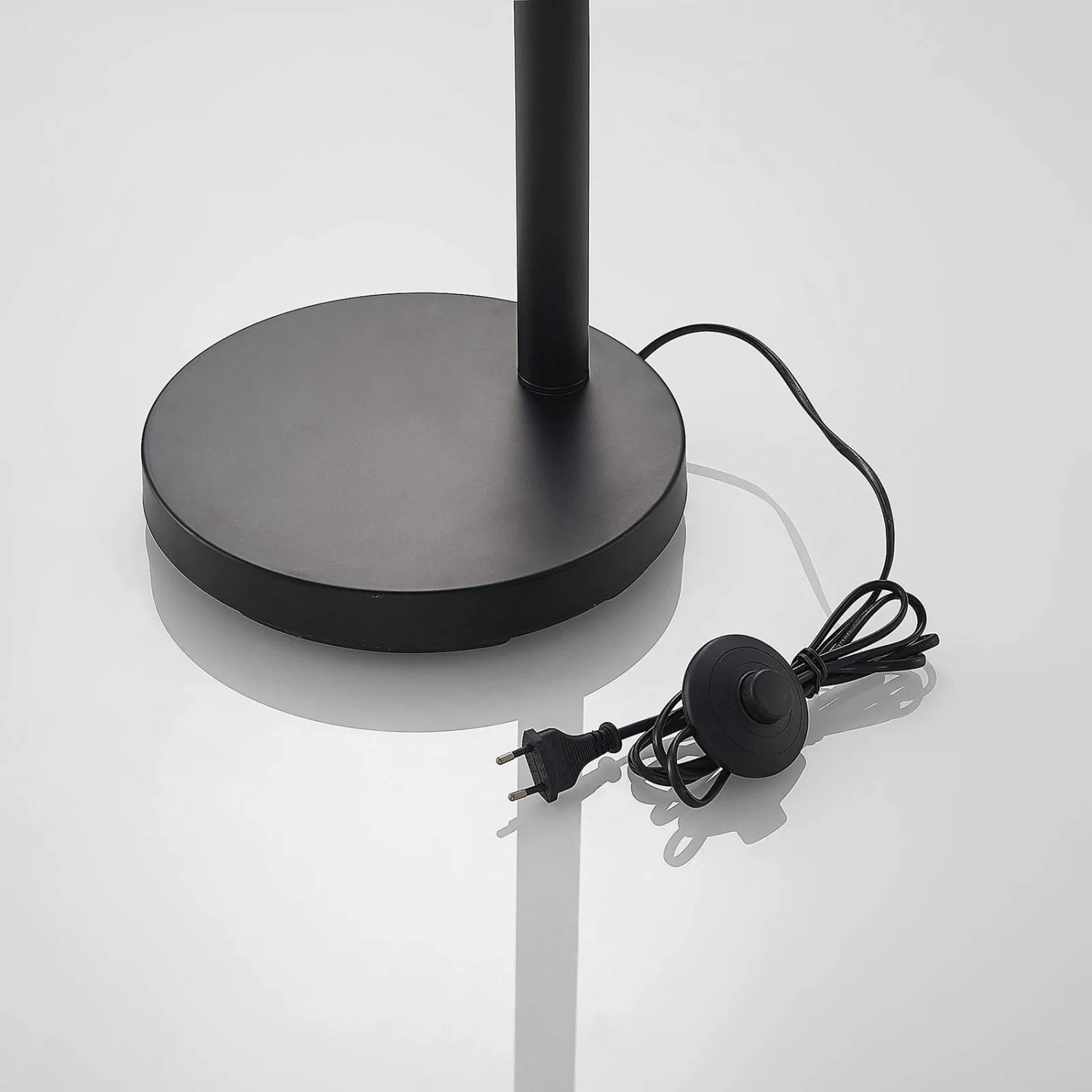 Detailaufnahme: Schwarze Lindby Bogenleuchte Jewa Stehlampe, runder Fuß, Kabel und Fußschalter.