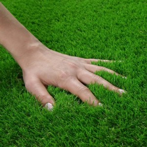 Nahaufnahme: Hand berührt weichen, grünen Karat Kunstrasen Vita 40mm. Ideal für Garten, Balkon und Terrasse.