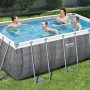 Bestway Frame Pool-Set Power Steel in Rattan-Optik, eckig, mit badenden Personen im Garten.