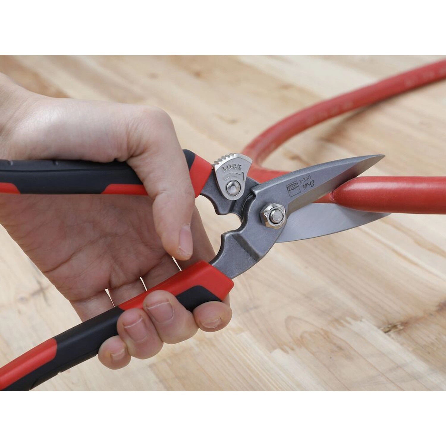 Erdi Combi-Schere D52-2 schneidet ein rotes Rohr. Zange mit rot-schwarzem Griff.