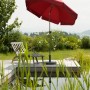 Dunkelroter Schneider Balkonschirm Aquila Ø 200 cm mit Push-Up Mechanik neben einem Gartenteich.
