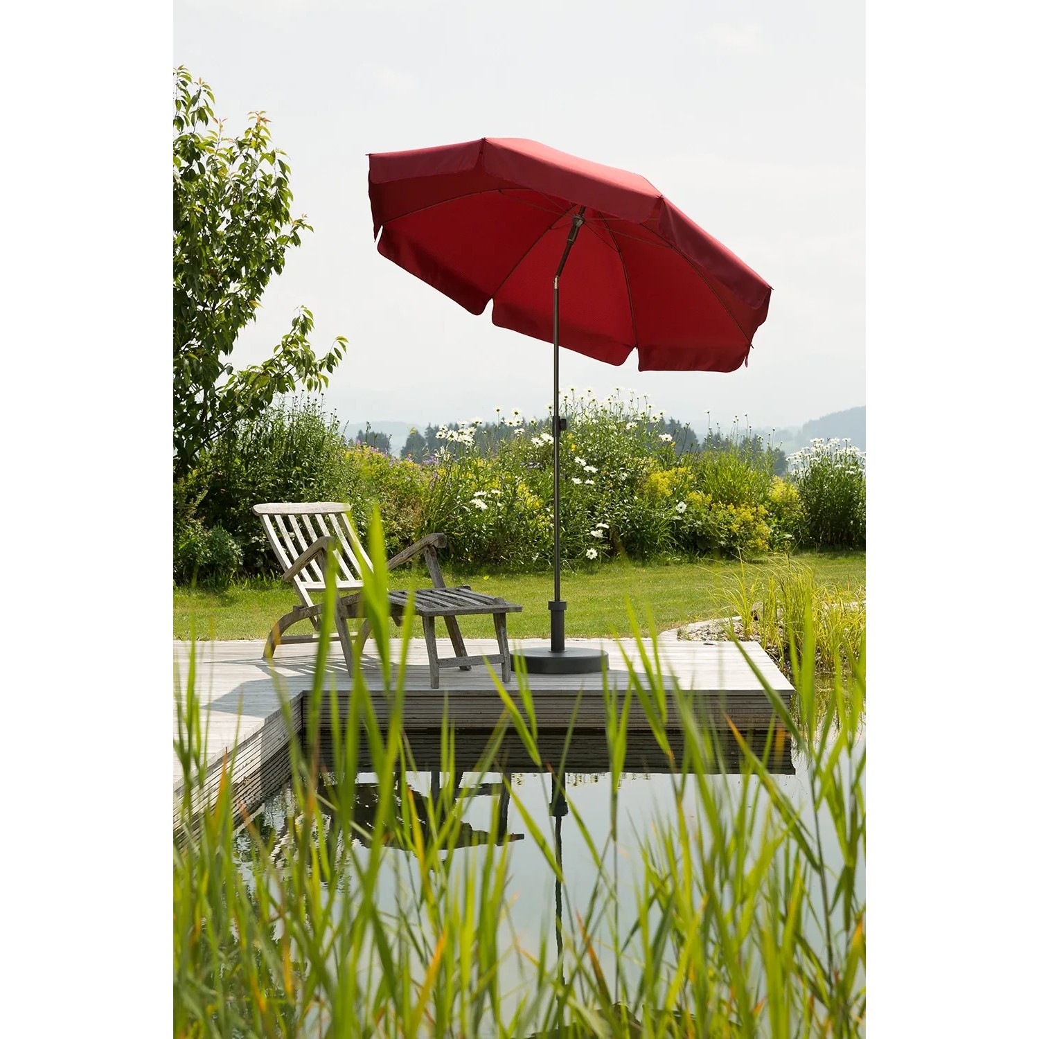 Dunkelroter Schneider Balkonschirm Aquila Ø 200 cm mit Push-Up Mechanik neben einem Gartenteich.