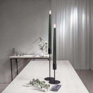 Zwei dunkelgrüne Star Trading LED Stabkerzen FLAMME SLIM mit 3D Flamme und Fernbedienung auf einem Holztisch.