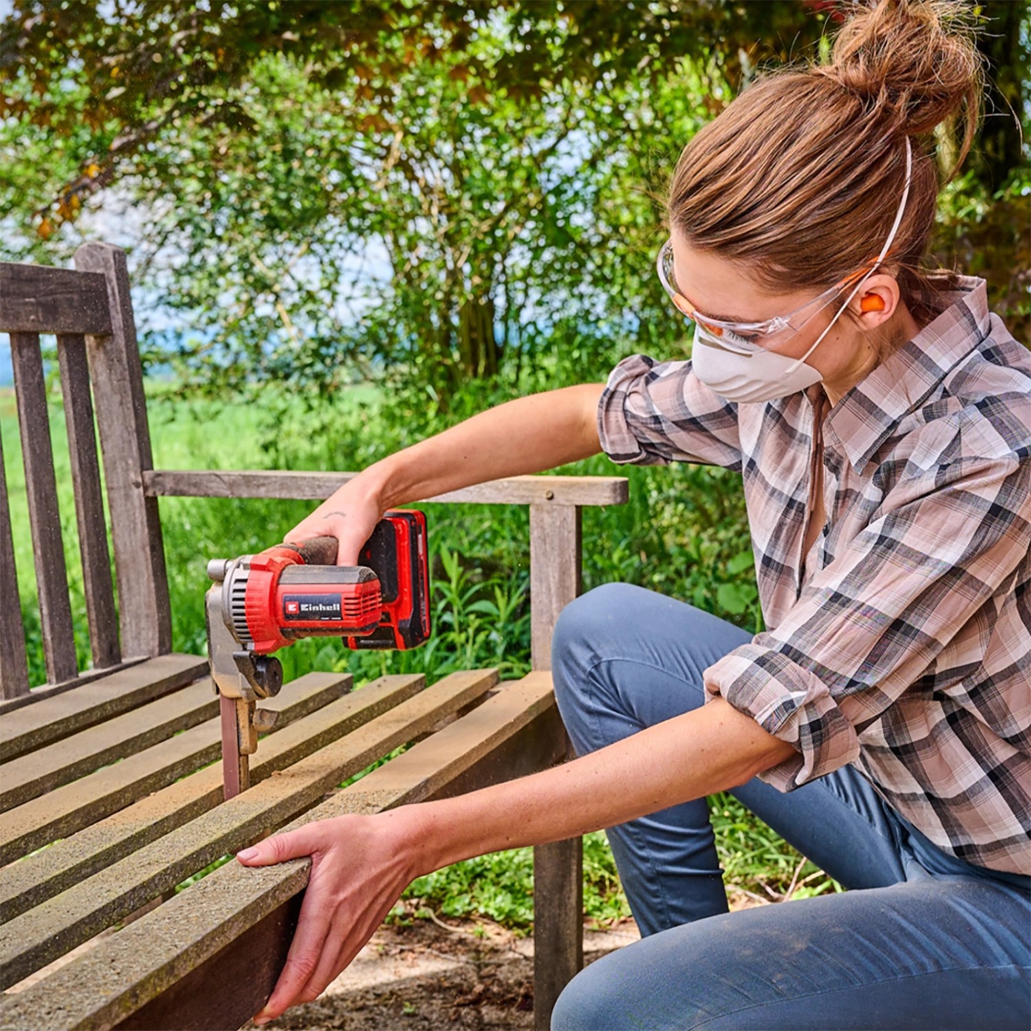 Frau schleift Holzbank mit roter Einhell Akku-Bandfeile TE-BF 18 V Li-Solo. Akkugerät mit Schleifband.