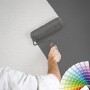 Mann streicht weiße Raufaser Tapete mit Farbroller grau. Farbfächer im Bild.