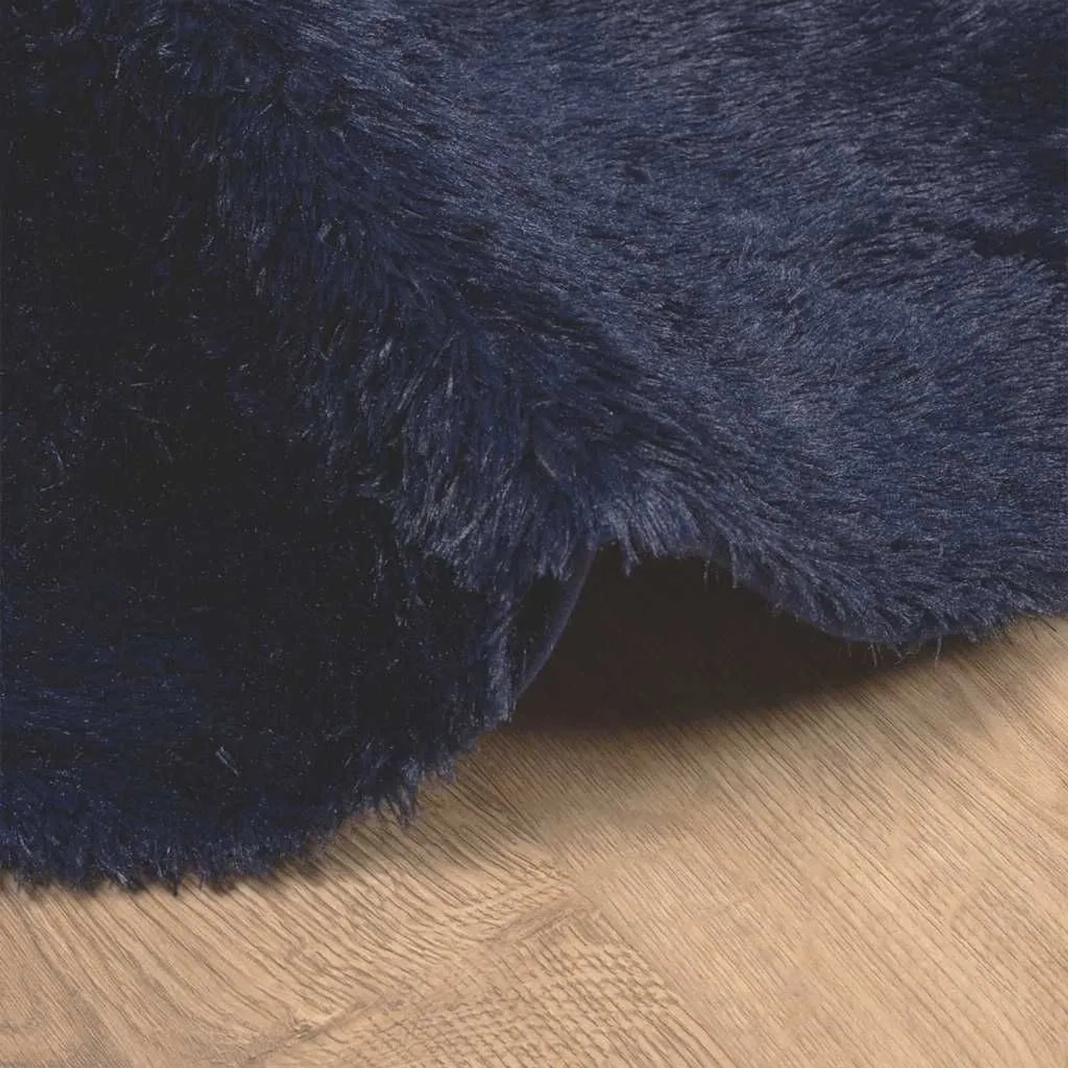Detailansicht eines marineblauen Shaggy Hochflorteppichs aus Polyester auf hellem Holzfußboden. Weiche, dichte Textur.