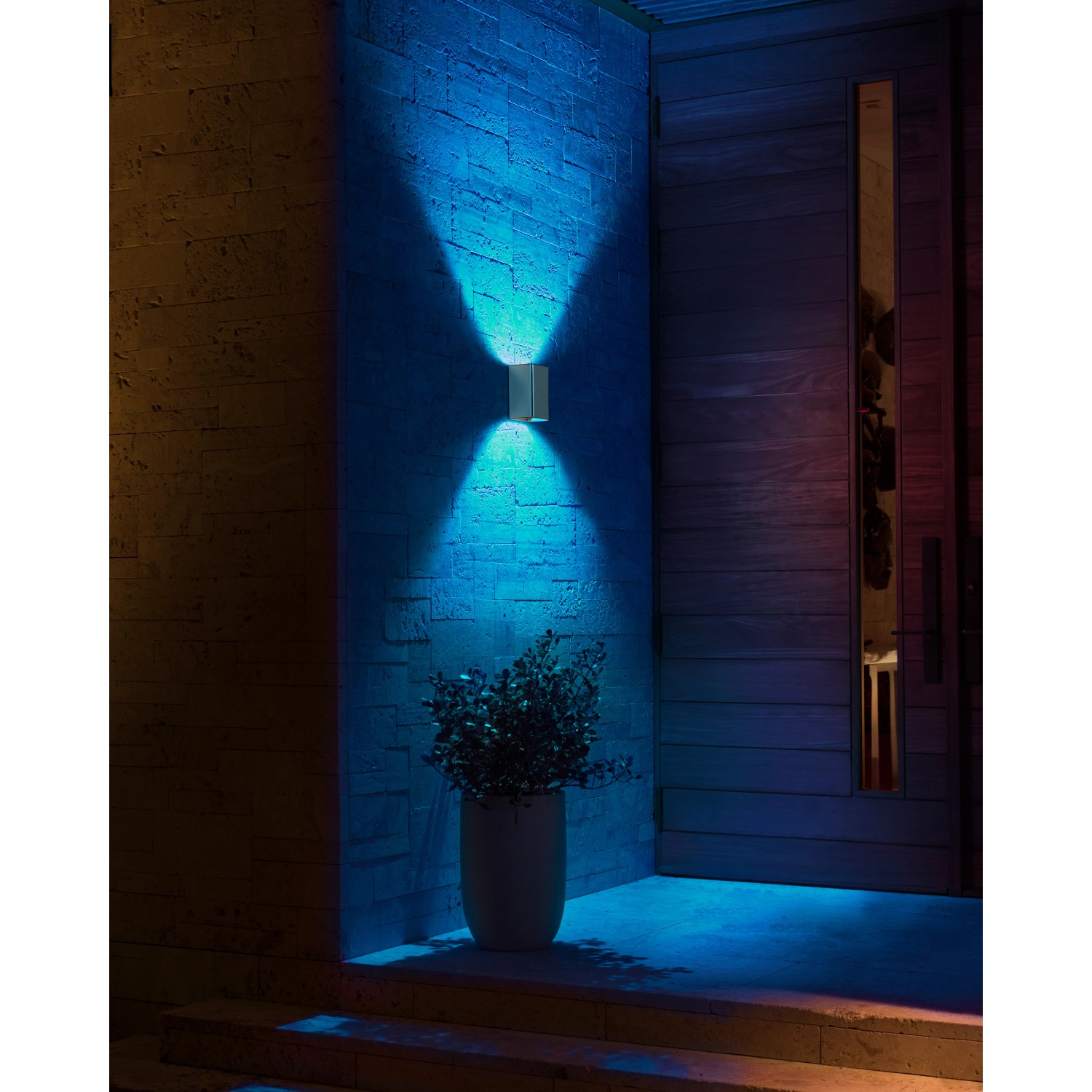 Silberne Philips Hue Resonate LED-Außenwandleuchte mit blauem Lichtschein an einer Hauswand.
