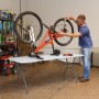 Weißer Lifetime Klapptisch (183x76cm) mit Mann, der ein Fahrrad repariert. Gartentisch für Reparaturen.