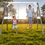 Axi Doppelschaukel aus Holz in Grau und Weiß mit zwei Kindern beim Schaukeln im Garten.