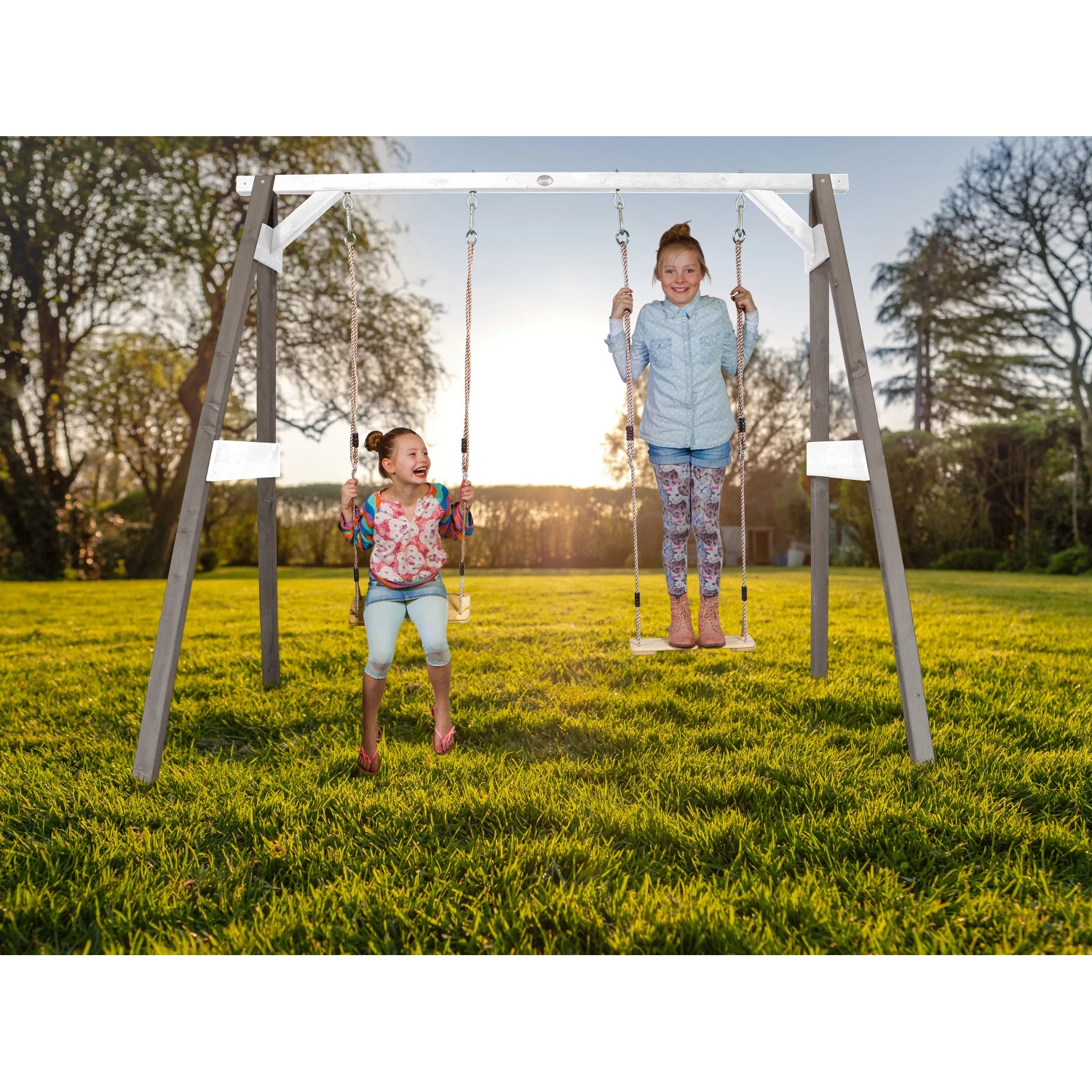 Axi Doppelschaukel aus Holz in Grau und Weiß mit zwei Kindern beim Schaukeln im Garten.