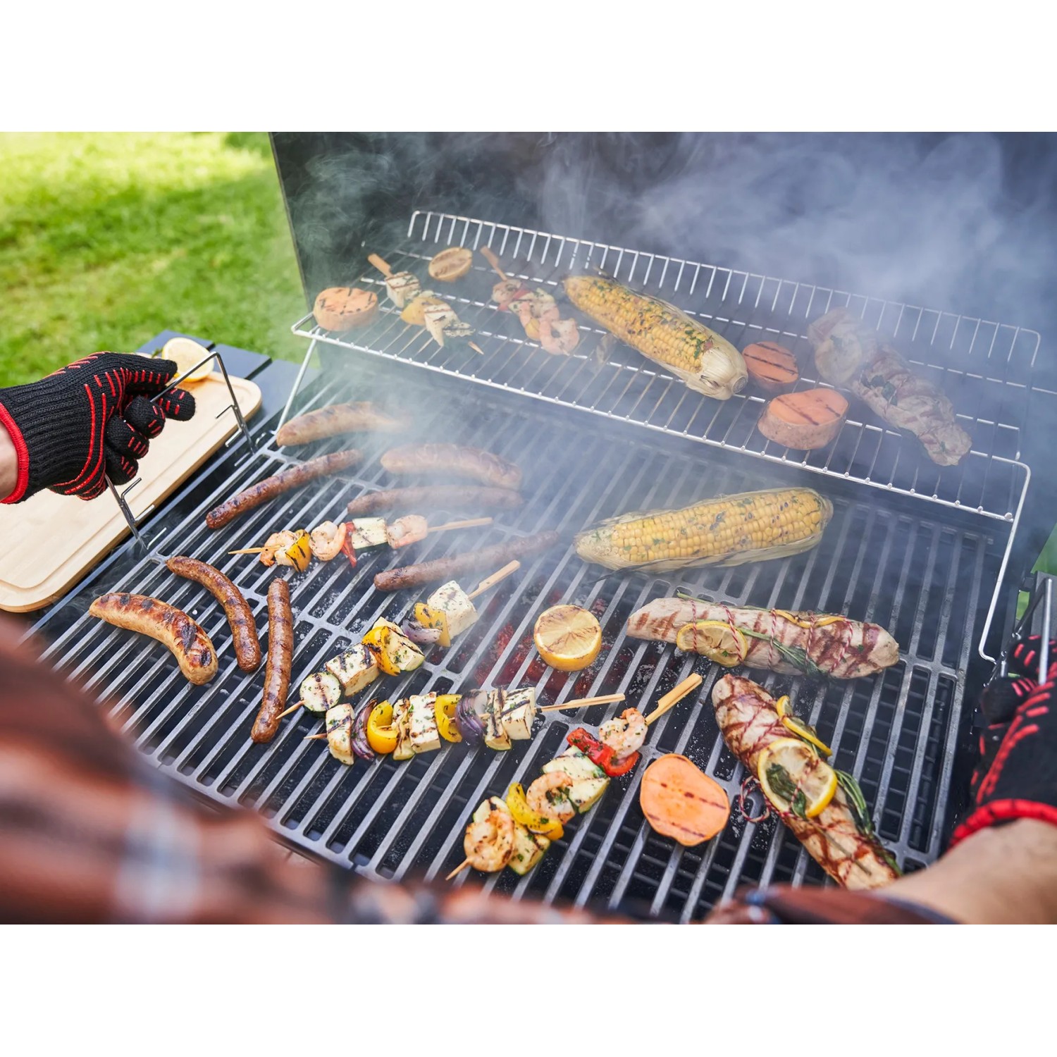 Char-Broil Holzkohlegrill L mit Grillgut: Würstchen, Maiskolben und Spieße auf dem Rost.