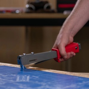 Arrow Hammertacker HT55 in Nutzung: Hand tackert blaue Folie auf Holz. Ideal für Dachdeckerarbeiten.
