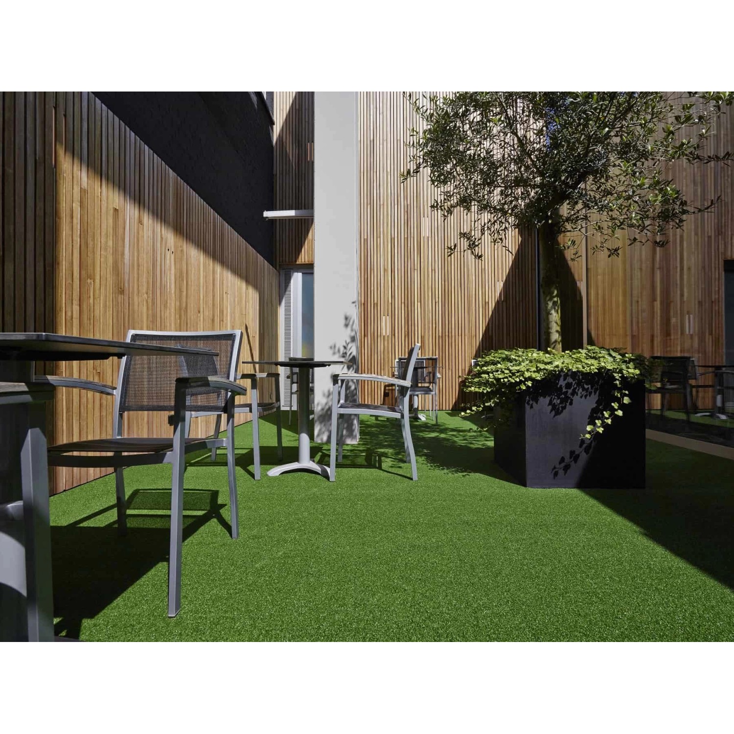 Primaflor Kunstrasen Summer B1, 2x2,5m, im Außenbereich mit Gartenmöbeln und Holzwand.