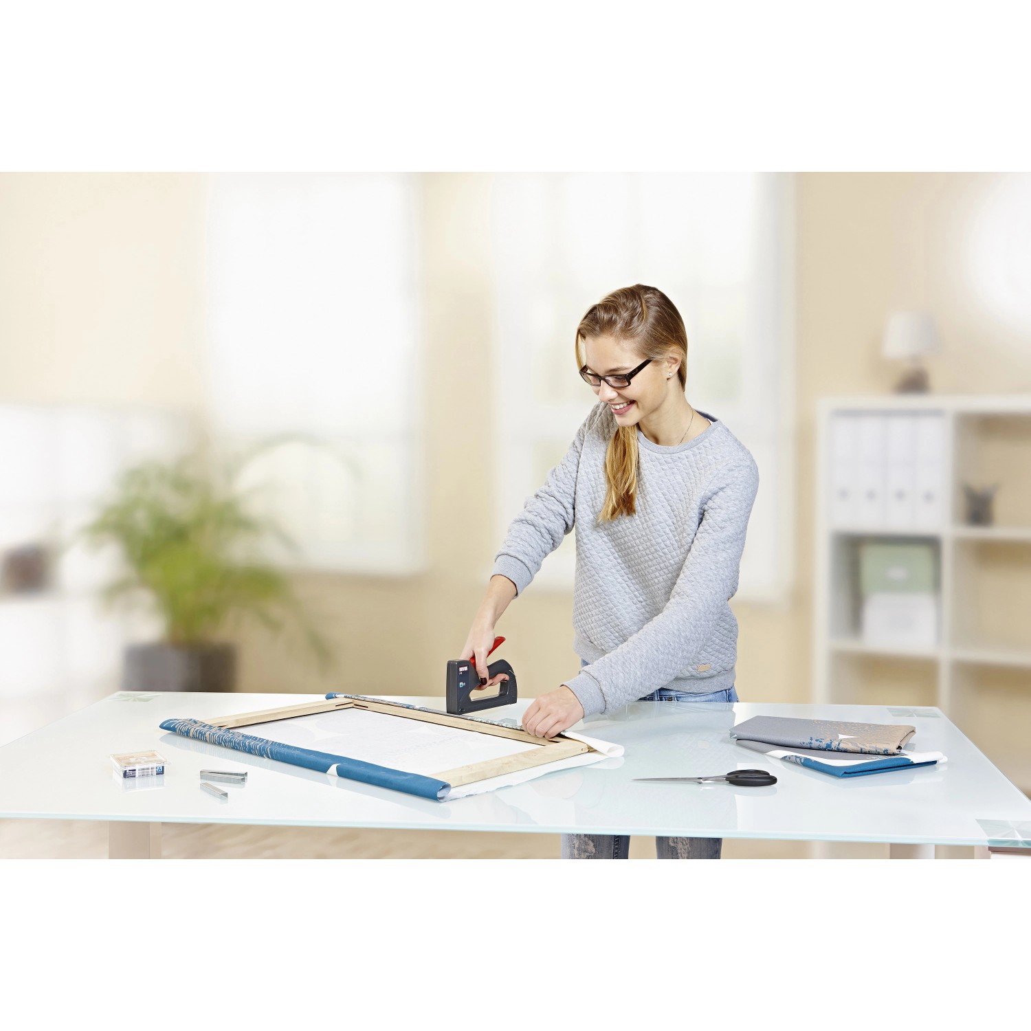 Frau tackert Leinwand mit Novus Handtacker J-13 (schwarz-rot).