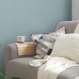 Blaue Vliestapete mit leichter Struktur an Wand hinter Sofa mit Kissen und Decke.
